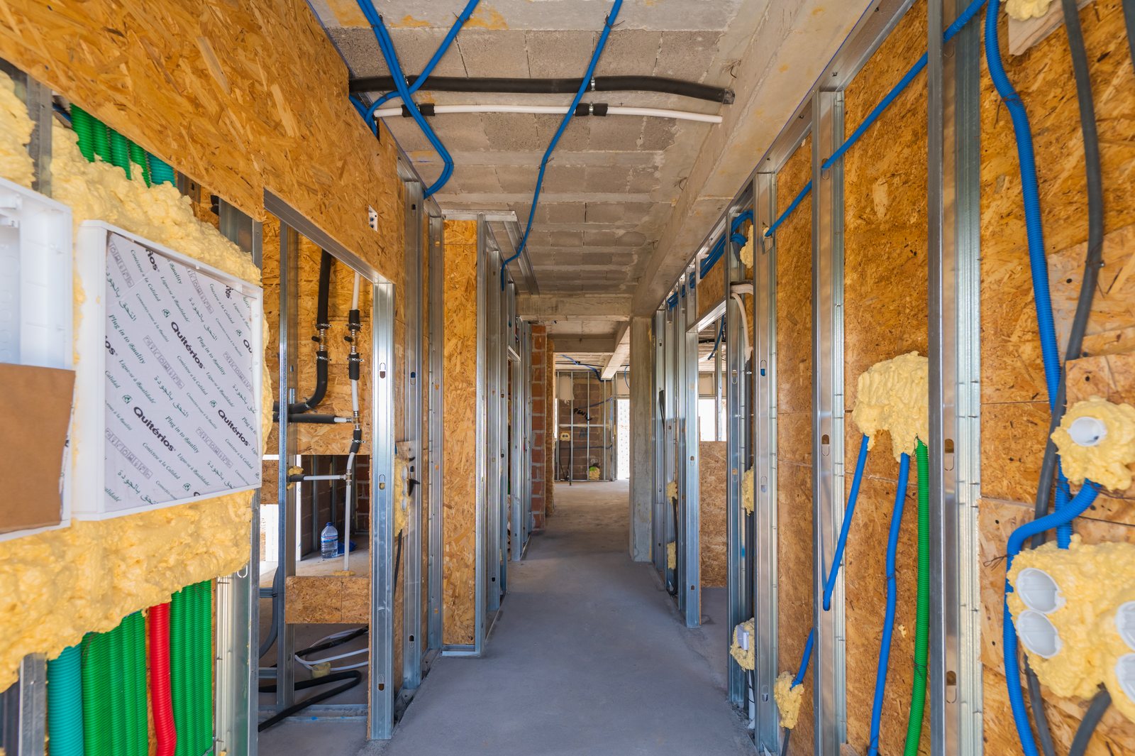 Corredor dos quartos em obra, com estrutura metálica, OSB e instalações à vista