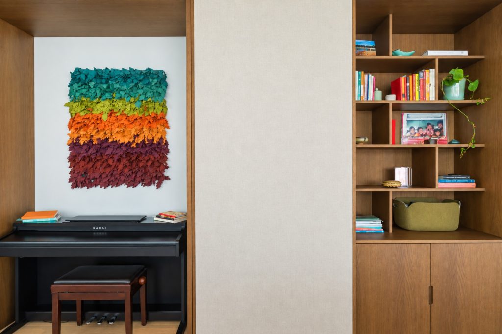 Interior de arquitetura com nicho em madeira, piano, obra têxtil colorida e estante embutida
