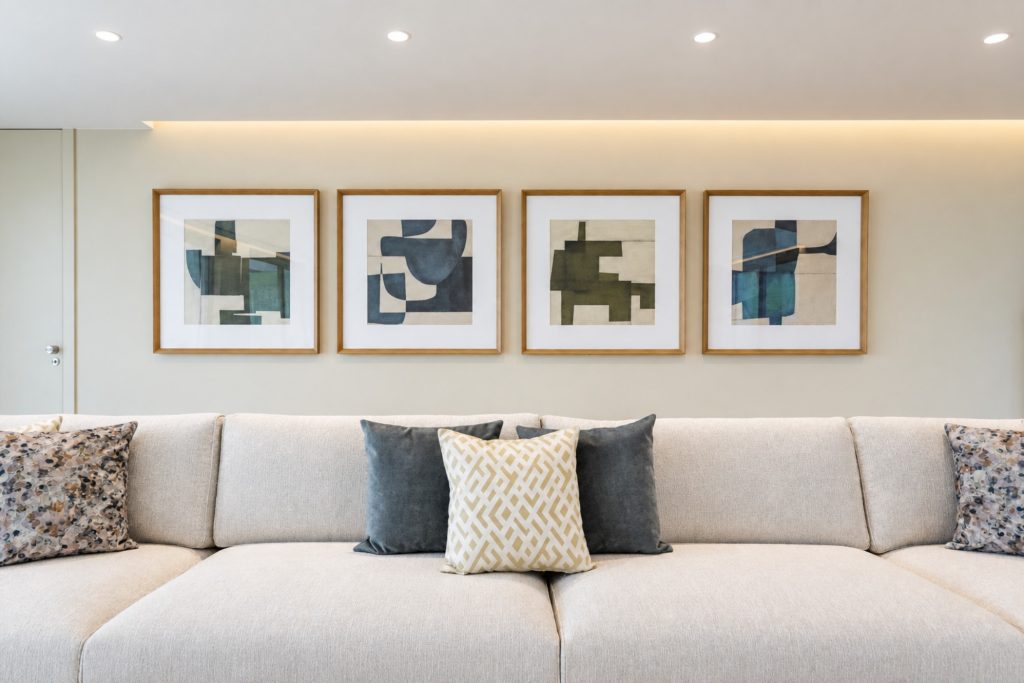 Pormenor de sala com quatro quadros abstratos sobre um sofá claro com almofadas