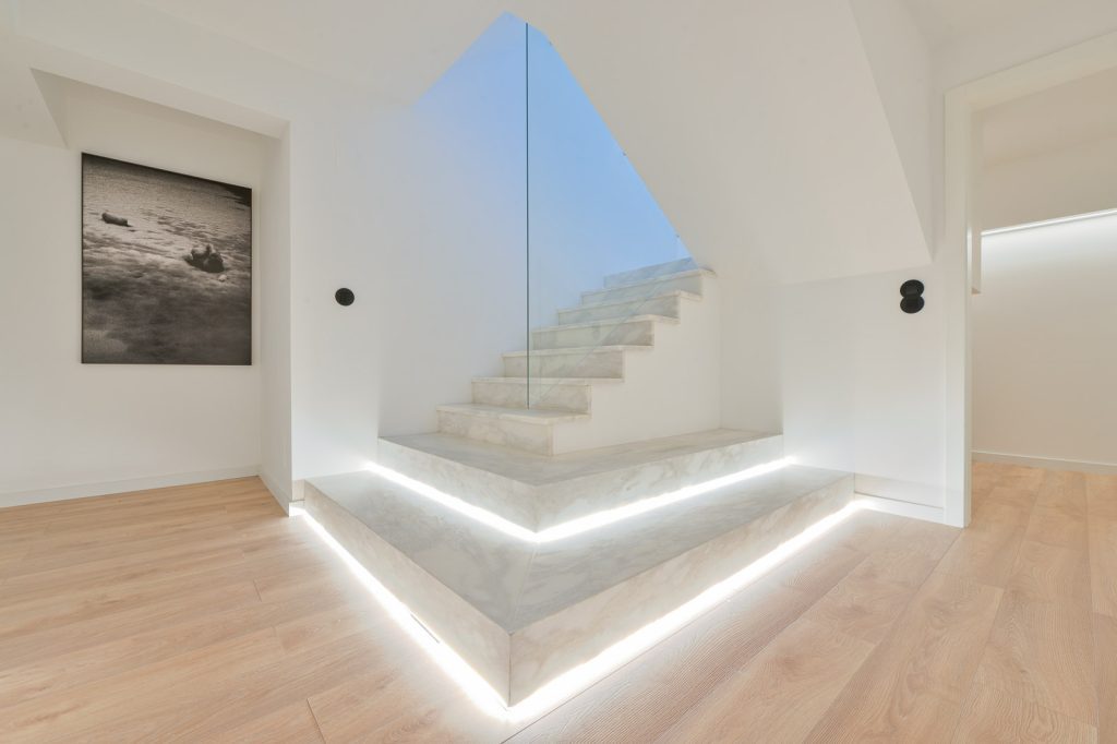 Escada em mármore branco com iluminação LED, guarda em vidro e claraboia