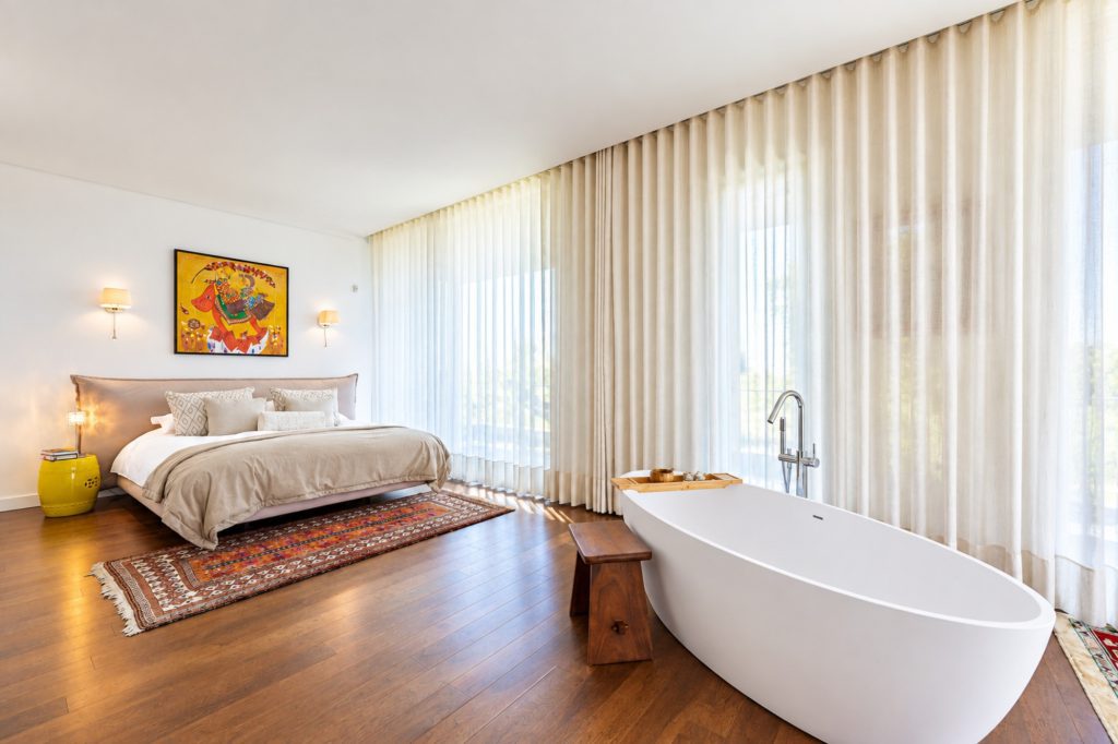 Suíte com cama de casal, banheira de pé livre e cortinas do chão ao teto