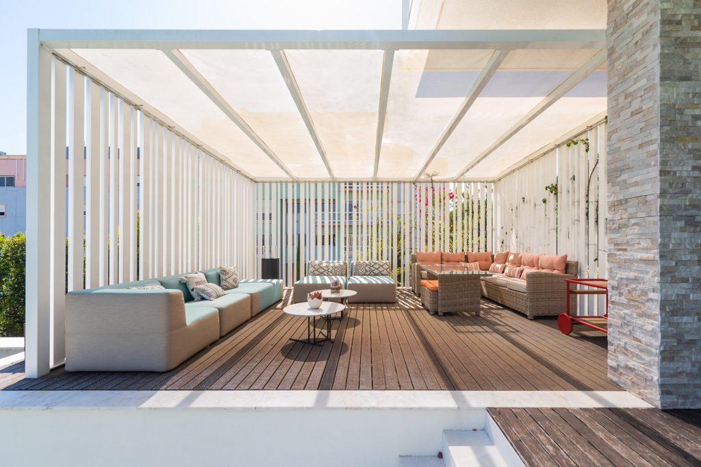 Pérgola branca com zona de estar exterior, sofás e deck de madeira